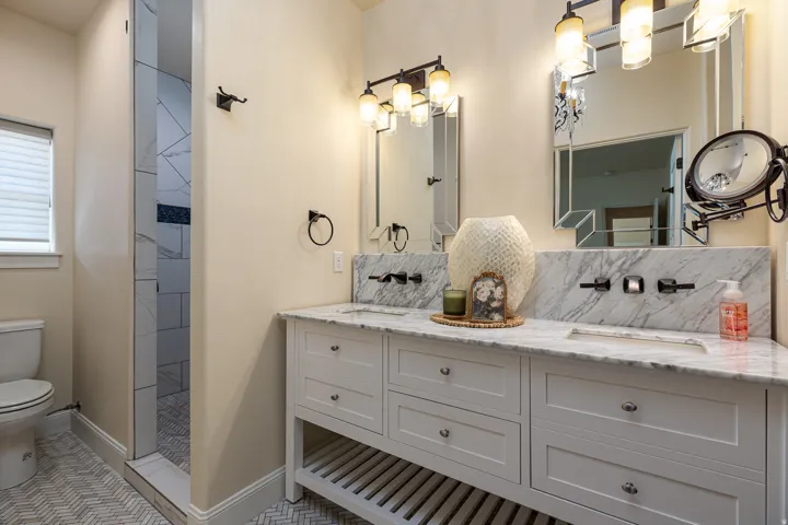 Dual vanity with white cabinetry, wall-mounted faucets, and a marble countertop