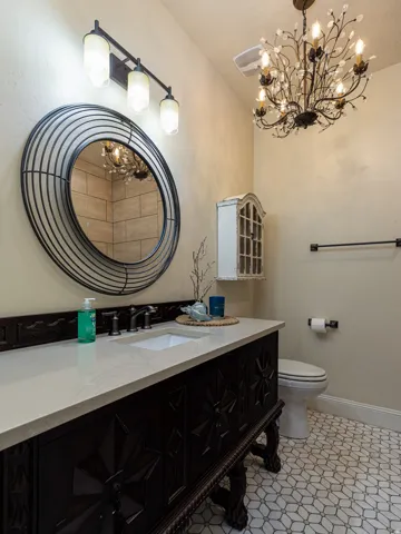 Powder room featuring a dark wood vanity with carved details, a light-toned countertop, a rectangular undermount sink, and a black-framed round mirror