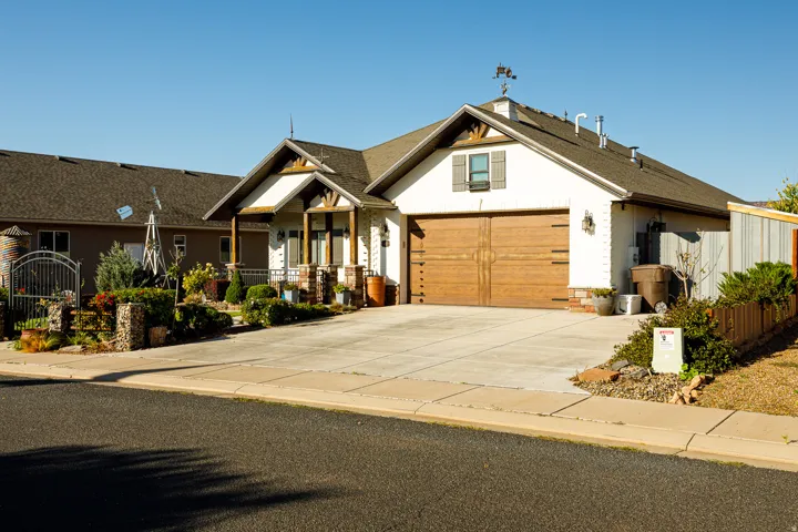 Single-story residence featuring a wood-finish garage door, white stucco exterior, and a gabled roofline