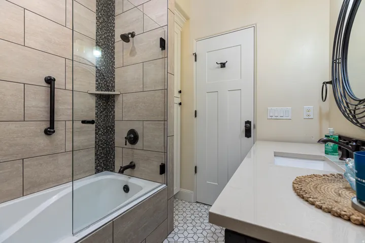 Bathroom featuring a bathtub with glass enclosure, beige rectangular wall tiles, and a mosaic tile accent strip