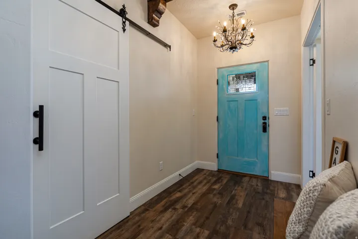 Entryway featuring a distressed turquoise front door with leaded glass, a bronze chandelier, wood-finish flooring, white baseboards, and a white barn door with black hardware