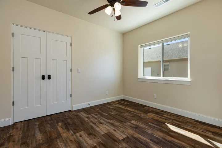 Room featuring wood-finish flooring, a ceiling fan with integrated lighting, a double-paned window, and double doors with dark hardware