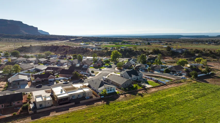 Aerial perspective showcasing a residential community with varying architectural styles, surrounded by expansive green fields and distant natural terrain