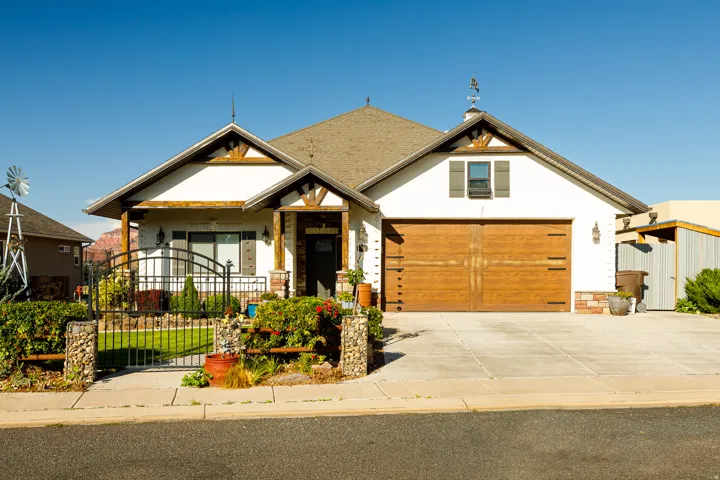 Stucco exterior with stone accents, wood-finish garage door, gabled roof, and a decorative front yard gate