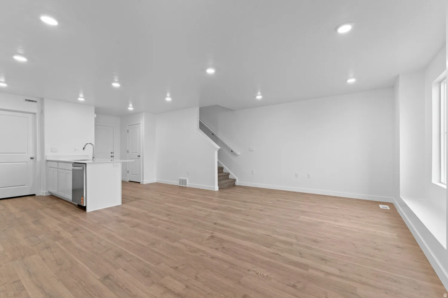 Open-concept living space with wood-finish flooring, recessed lighting, and a white kitchen island featuring a stainless steel dishwasher and gooseneck faucet