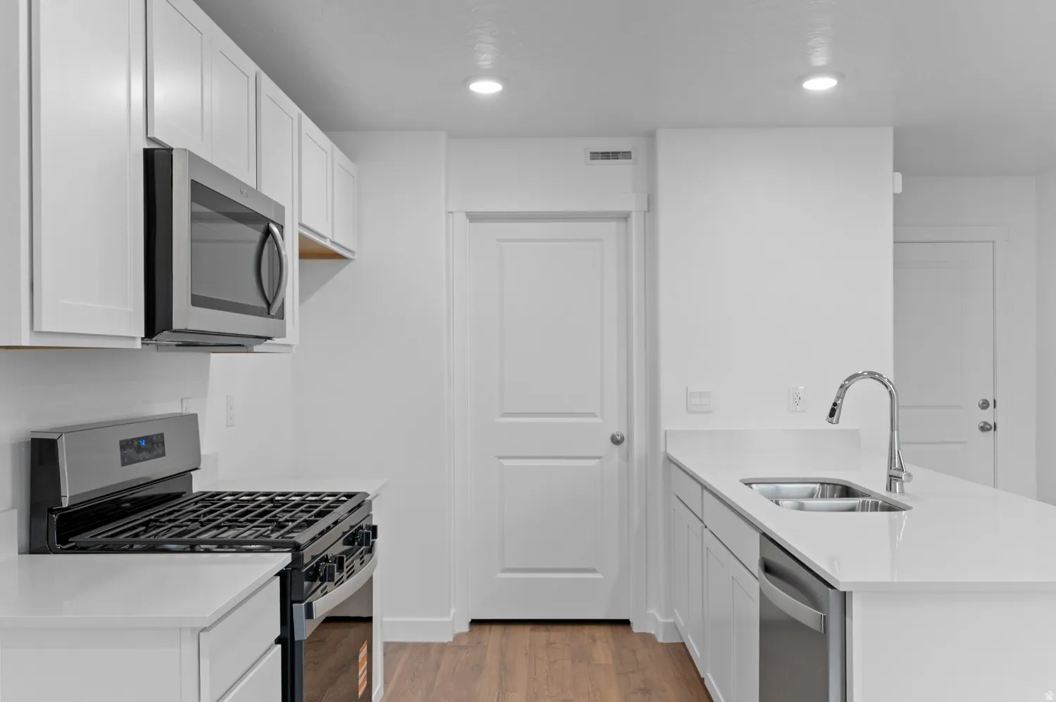 Modern kitchen featuring white shaker cabinetry, stainless steel appliances, light countertops, and wood-finish flooring