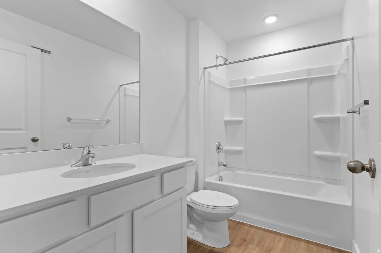 Full bathroom featuring a white vanity with an integrated sink, a large wall-mounted mirror, a tub/shower combination with white surround, and wood-finish flooring