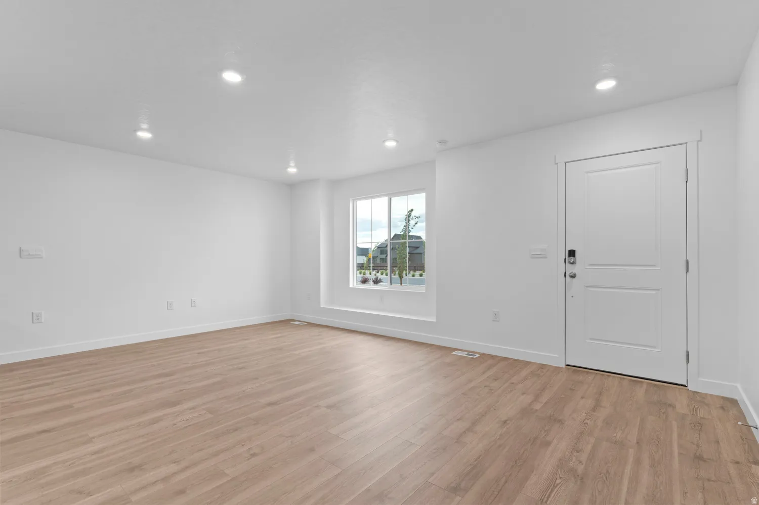 Spacious room featuring wood-finish flooring, recessed lighting, white walls, and a multi-pane window