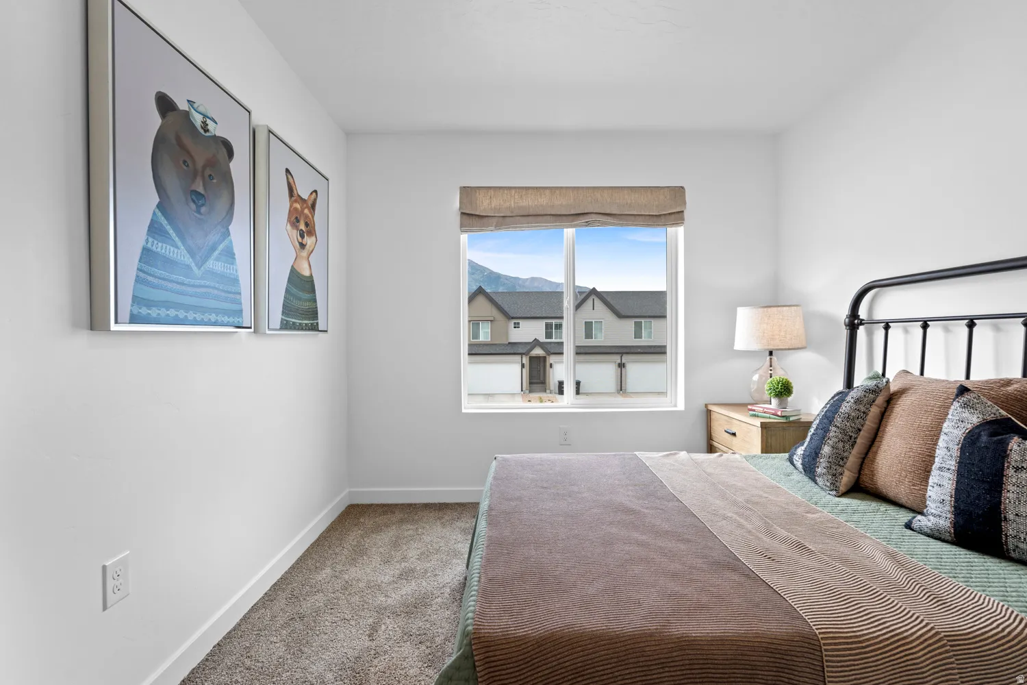 Bedroom featuring a window with integrated shade and mountain backdrop, complemented by a metal bed frame, wood-finish nightstand, and neutral carpeting