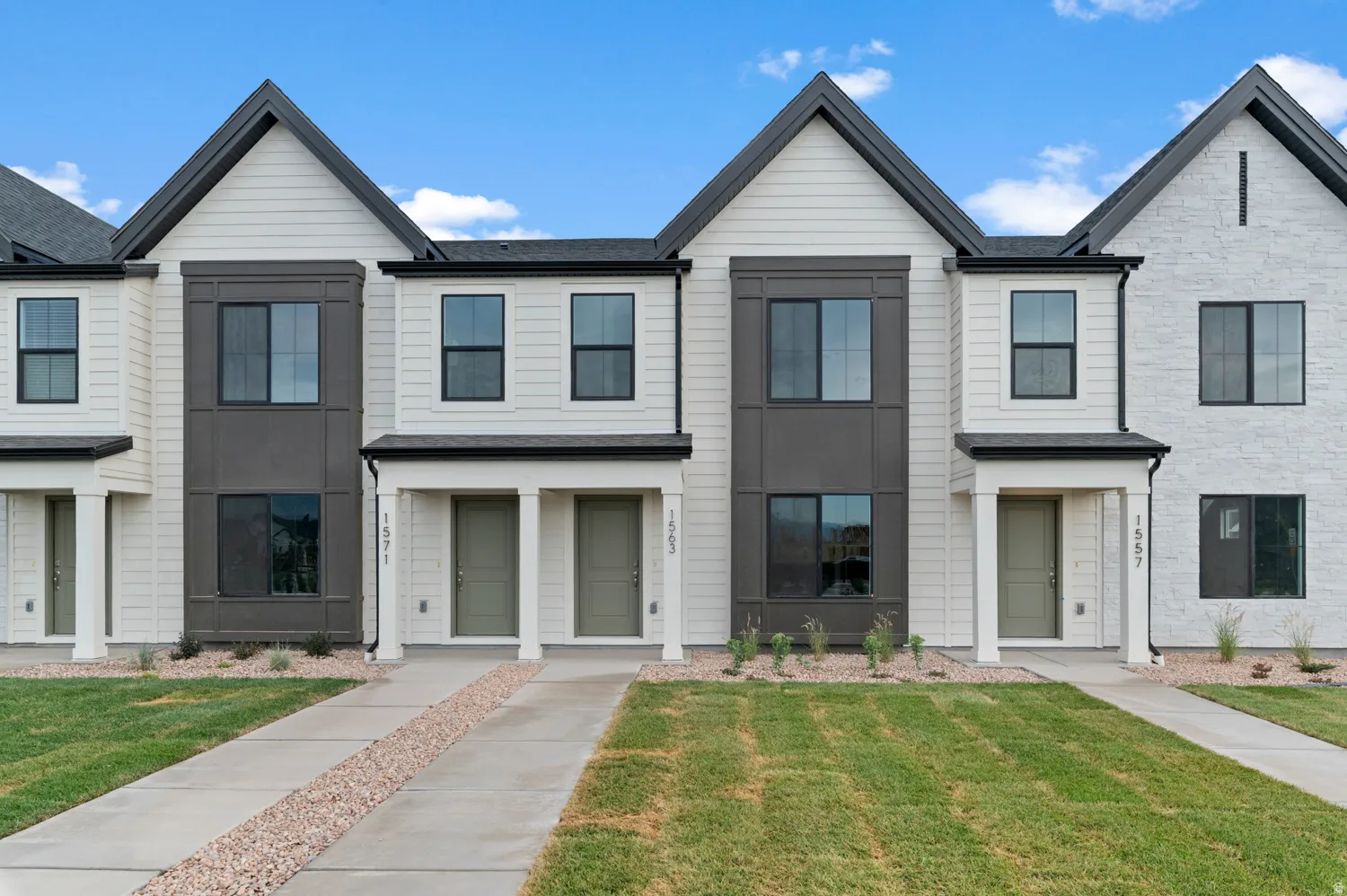 Modern townhome exterior featuring clean architectural lines, contrasting white siding with dark window frames, and a covered entry porch