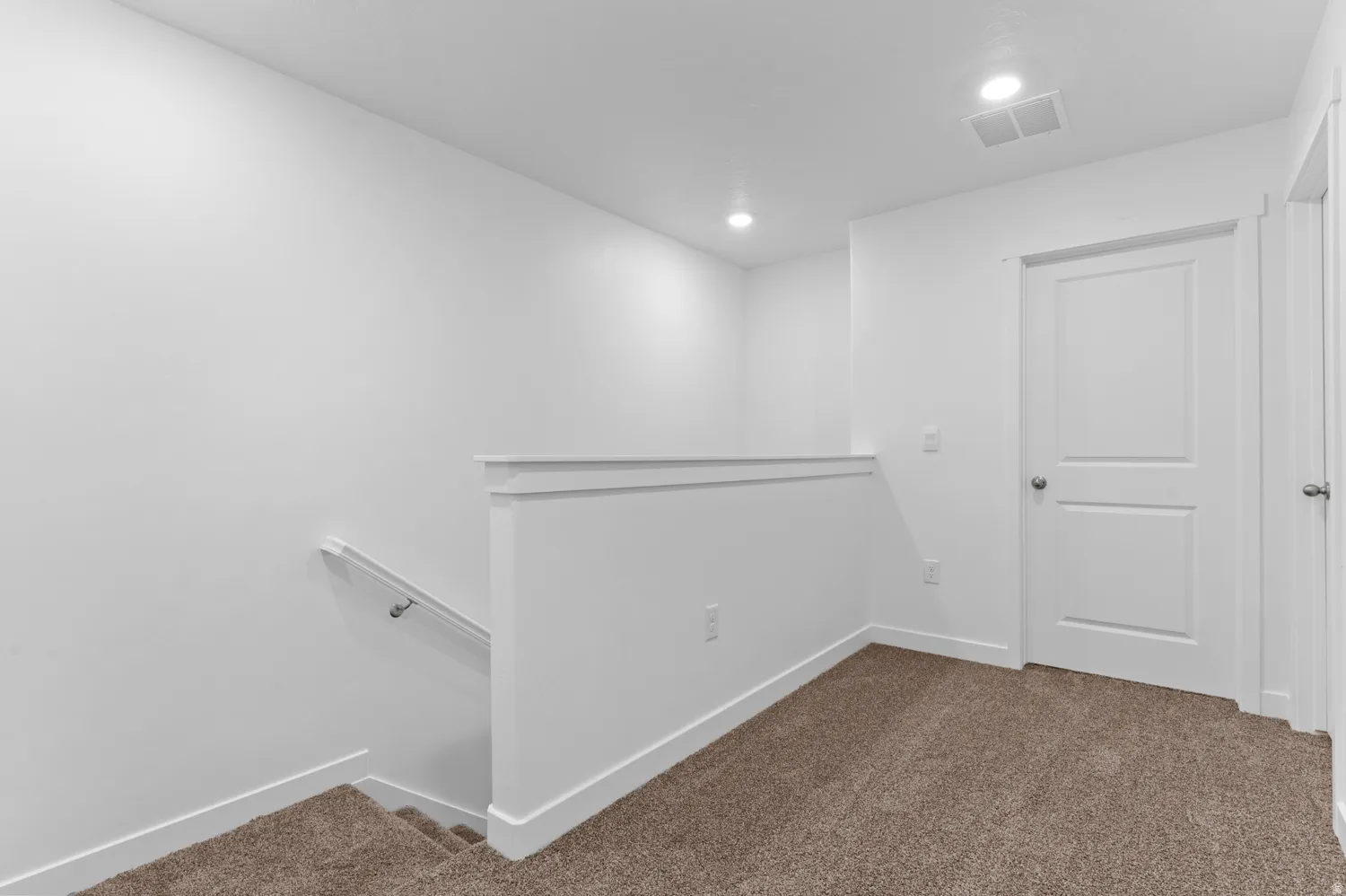 Carpeted landing featuring a white two-panel door, recessed lighting, and a white handrail along the staircase
