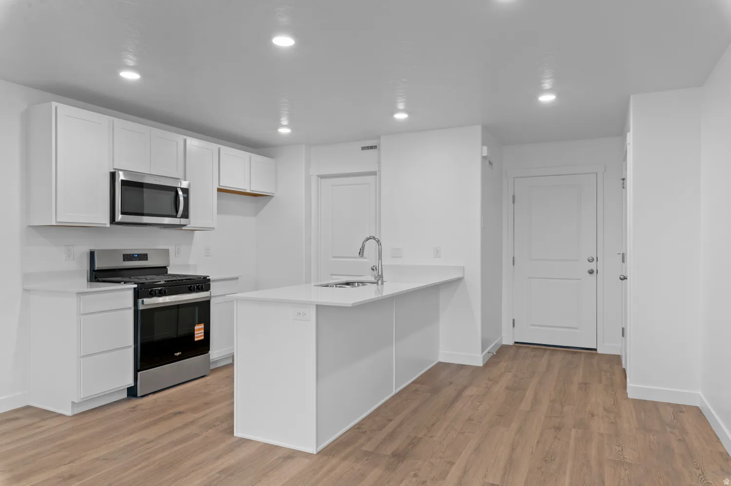 Kitchen featuring white shaker cabinetry, stainless steel appliances, a center island with sink, recessed lighting, and wood-finish flooring