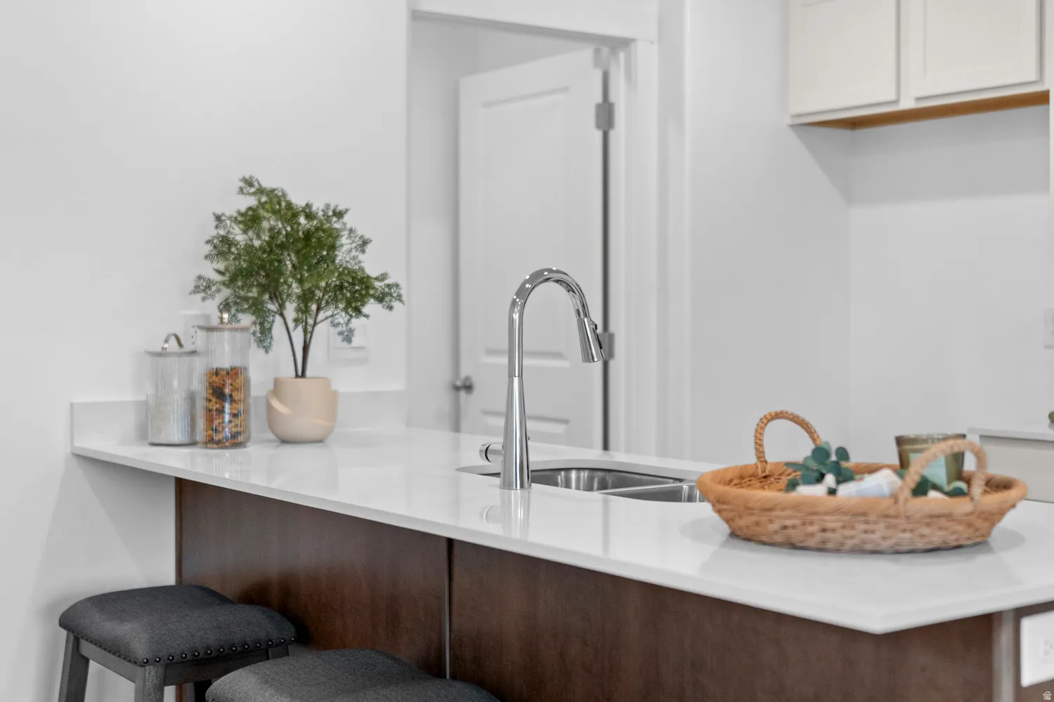 Kitchen island featuring a stainless steel sink with a high-arc faucet, light-toned countertop, and dark wood-finish cabinetry
