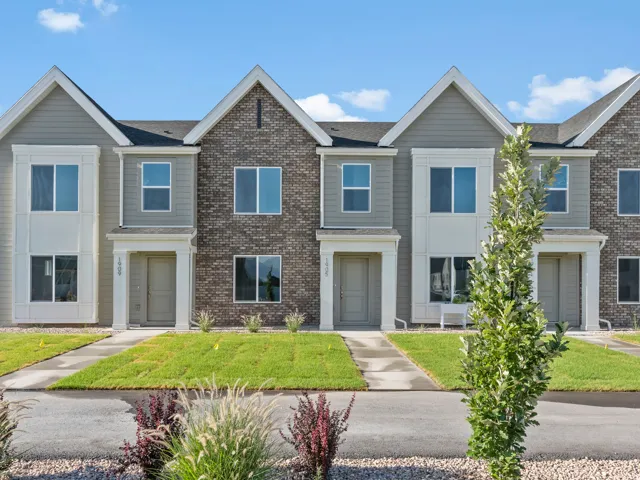 Townhome exterior featuring varied siding, brick accents, multiple windows, and a landscaped front yard with green grass and shrubbery
