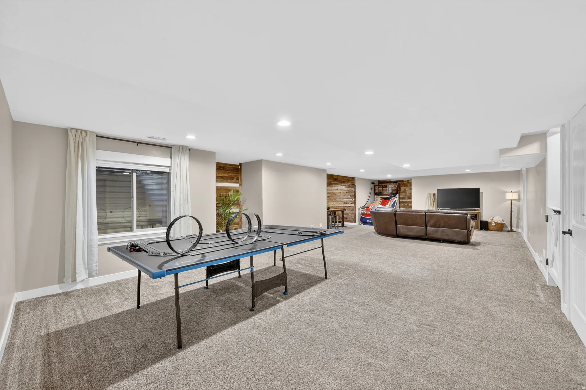 Spacious carpeted room featuring recessed lighting, a window with blinds, and an accent wall with horizontal wood paneling