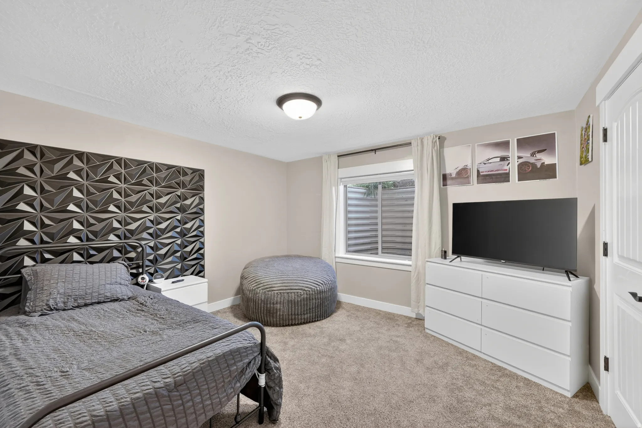 Carpeted bedroom featuring a textured accent wall, a flush-mount ceiling light fixture, a window with a window well, and a paneled interior door