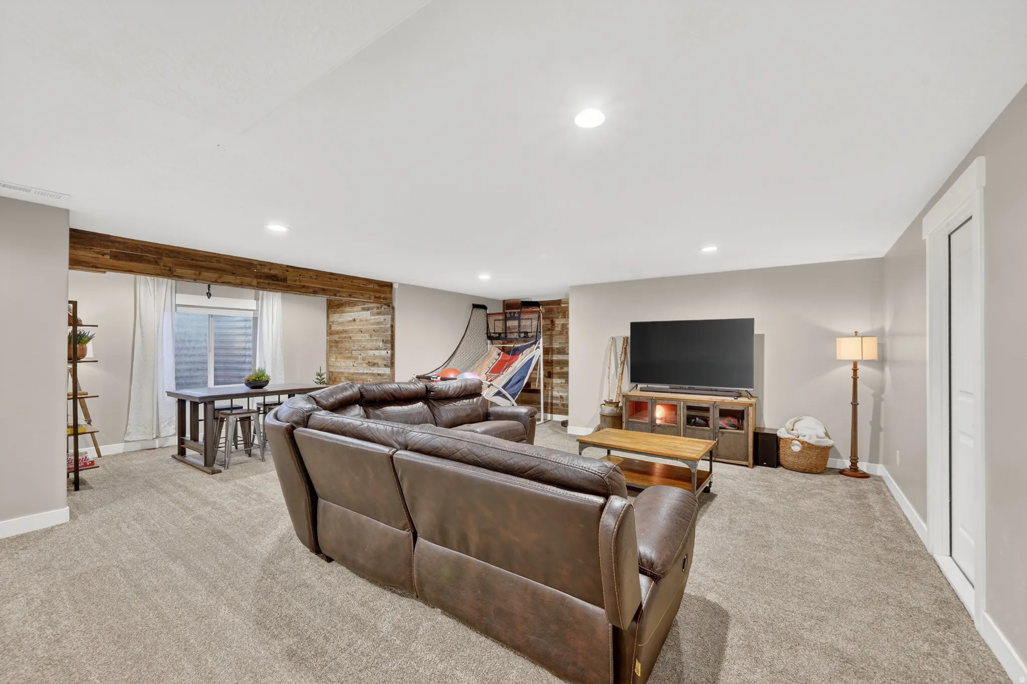 Spacious entertainment room featuring recessed ceiling lighting, light-toned carpet flooring, and a window with horizontal blinds