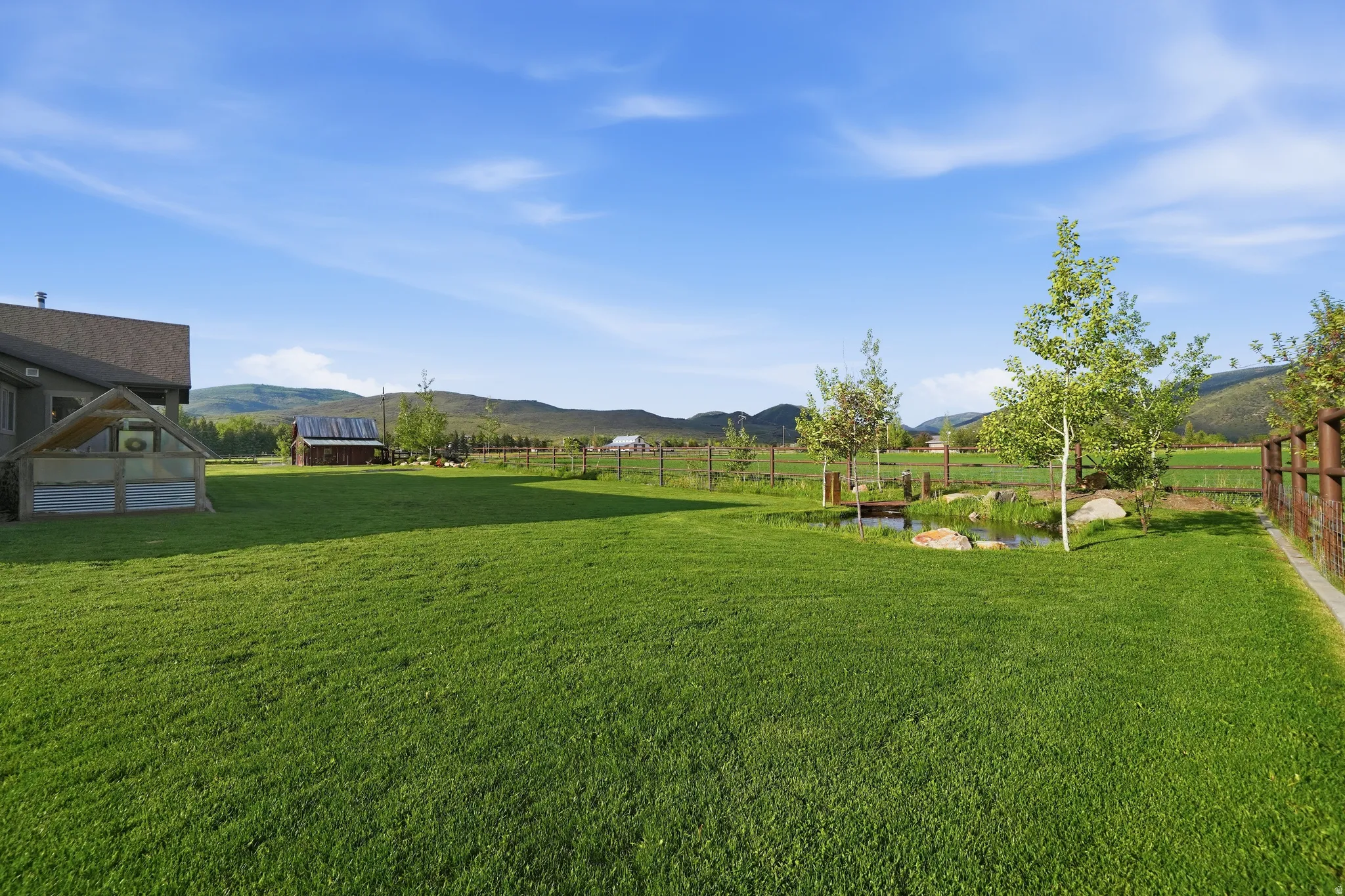 Expansive green lawn with a decorative pond feature, surrounded by mature trees and a wood fence