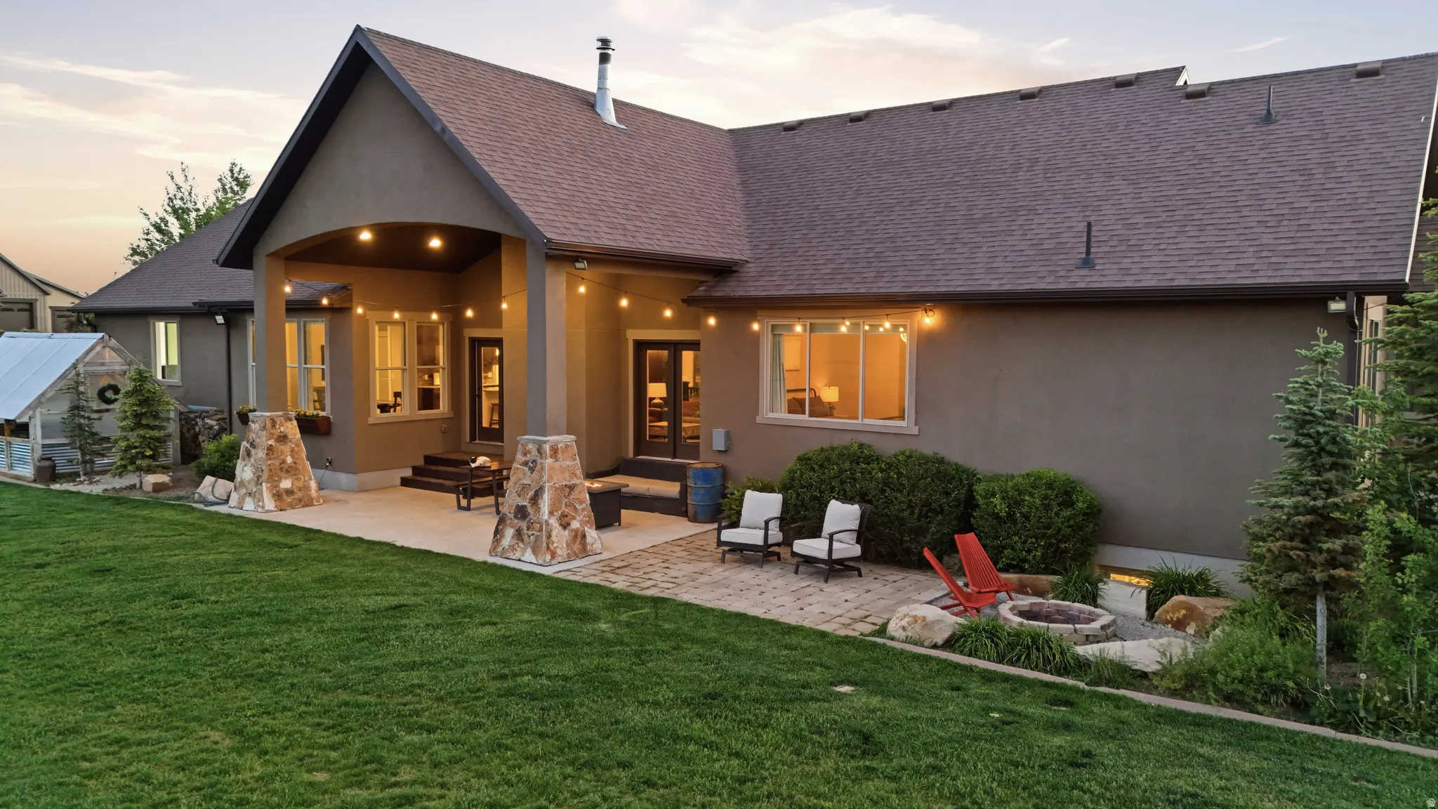Expansive backyard featuring a manicured lawn, a large paver patio, a covered patio area with recessed lighting, a built-in fire pit, and mature landscaping