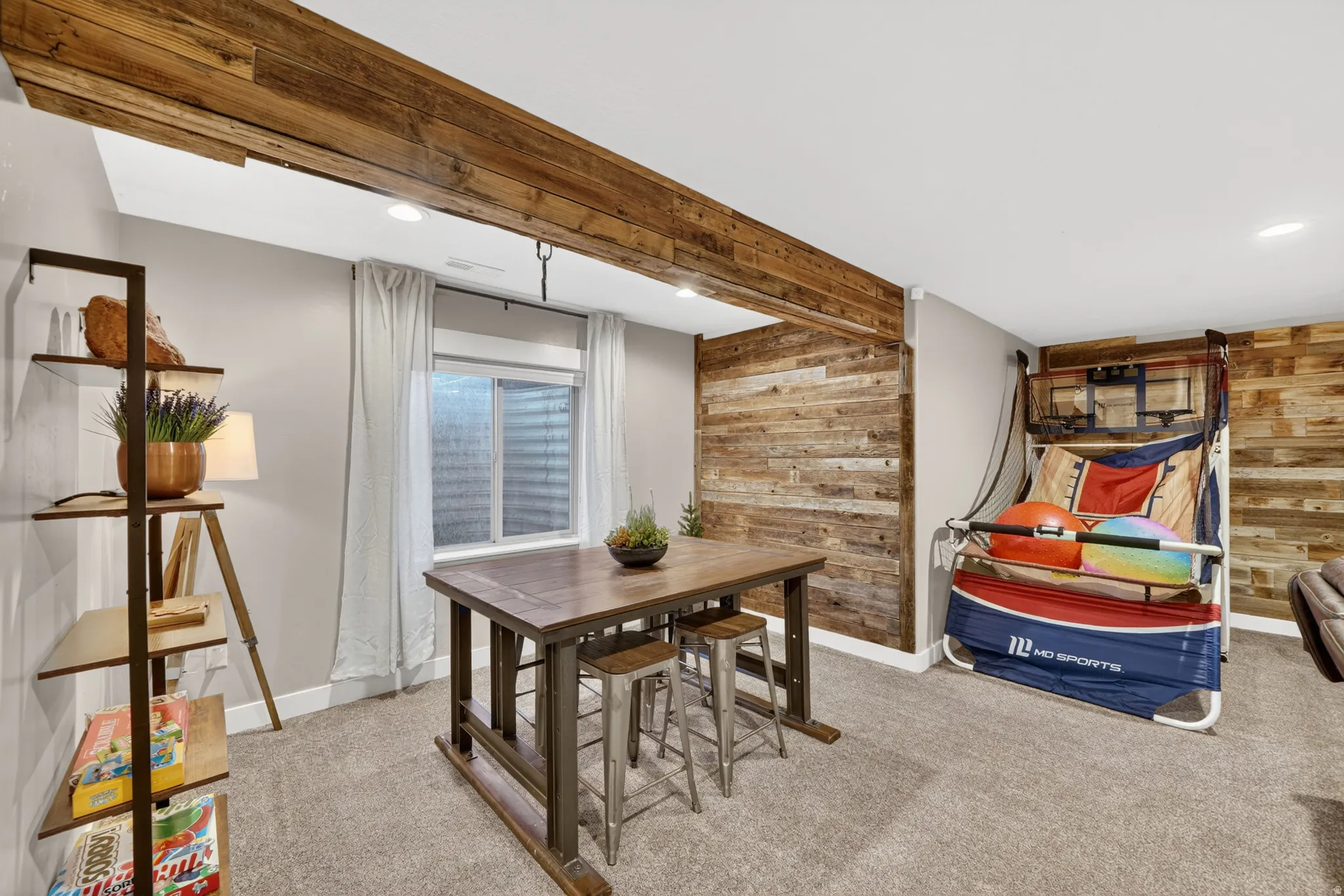Finished room featuring a wood-finish accent wall, exposed wood-finish beam, recessed lighting, window with privacy screen, and carpeted flooring