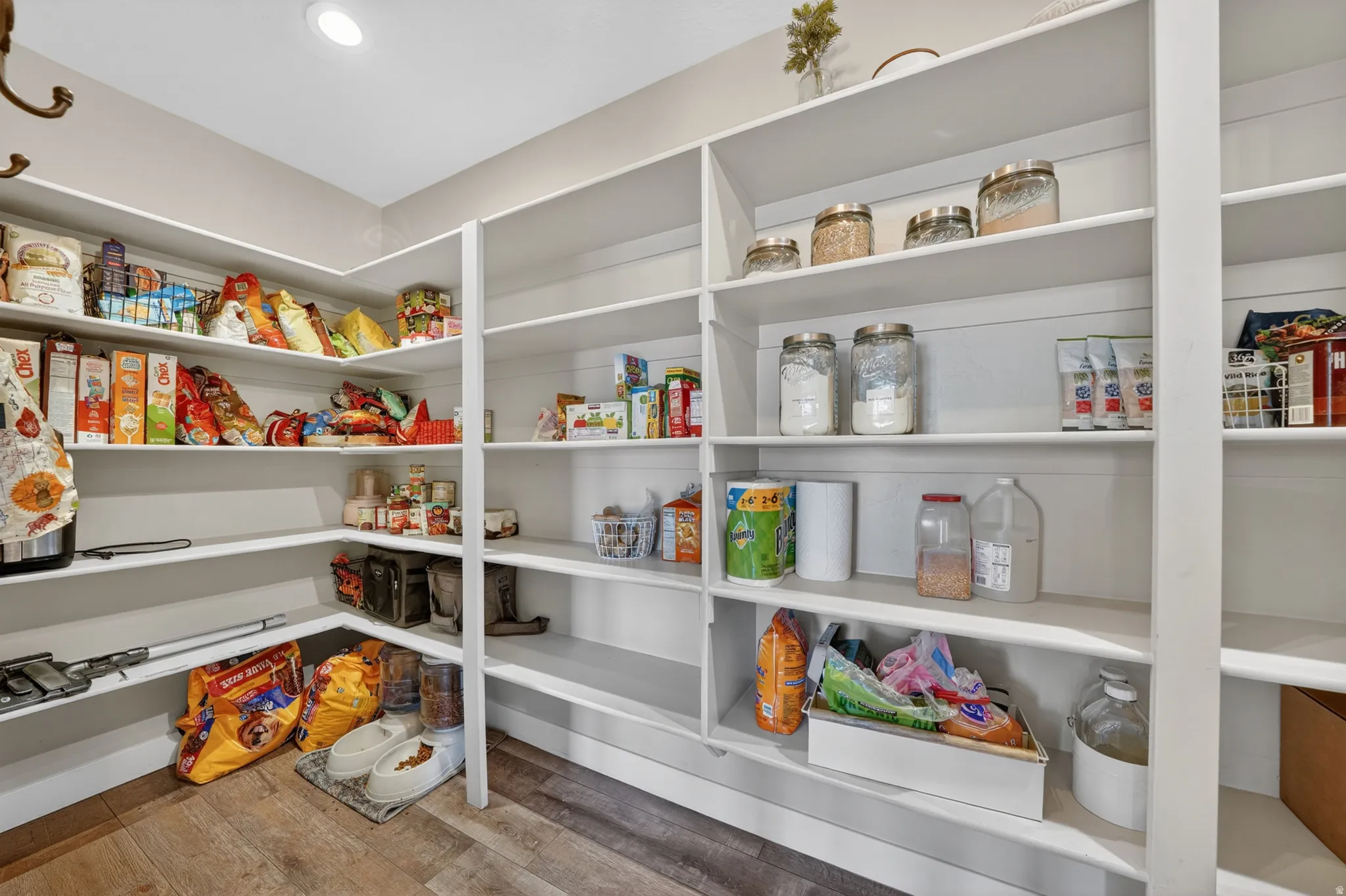 Spacious walk-in pantry featuring extensive white shelving, recessed lighting, and wood-finish flooring