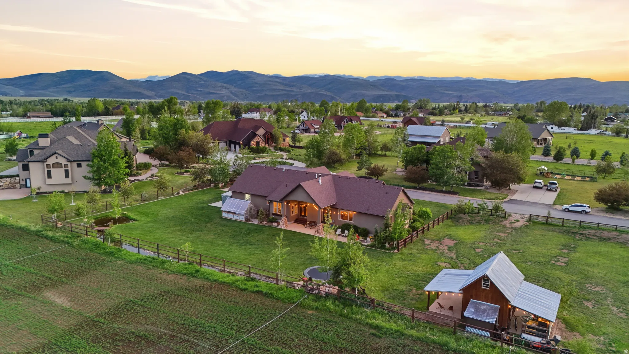Expansive property featuring a brown ranch-style residence with a covered patio, a detached barn-style structure with a metal roof, and a large manicured lawn