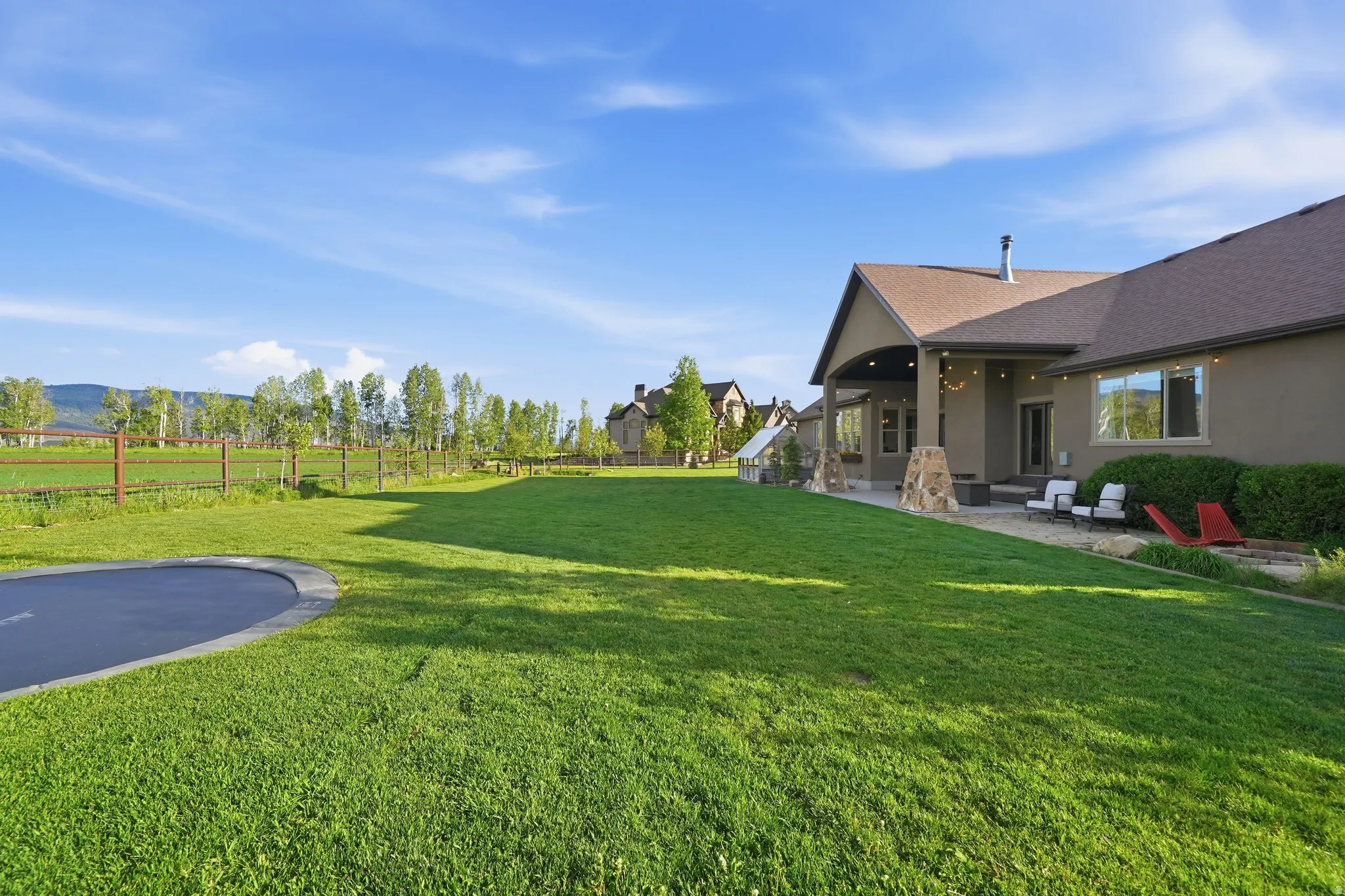 Expansive rear yard featuring a large lawn area, a built-in trampoline, and a covered patio