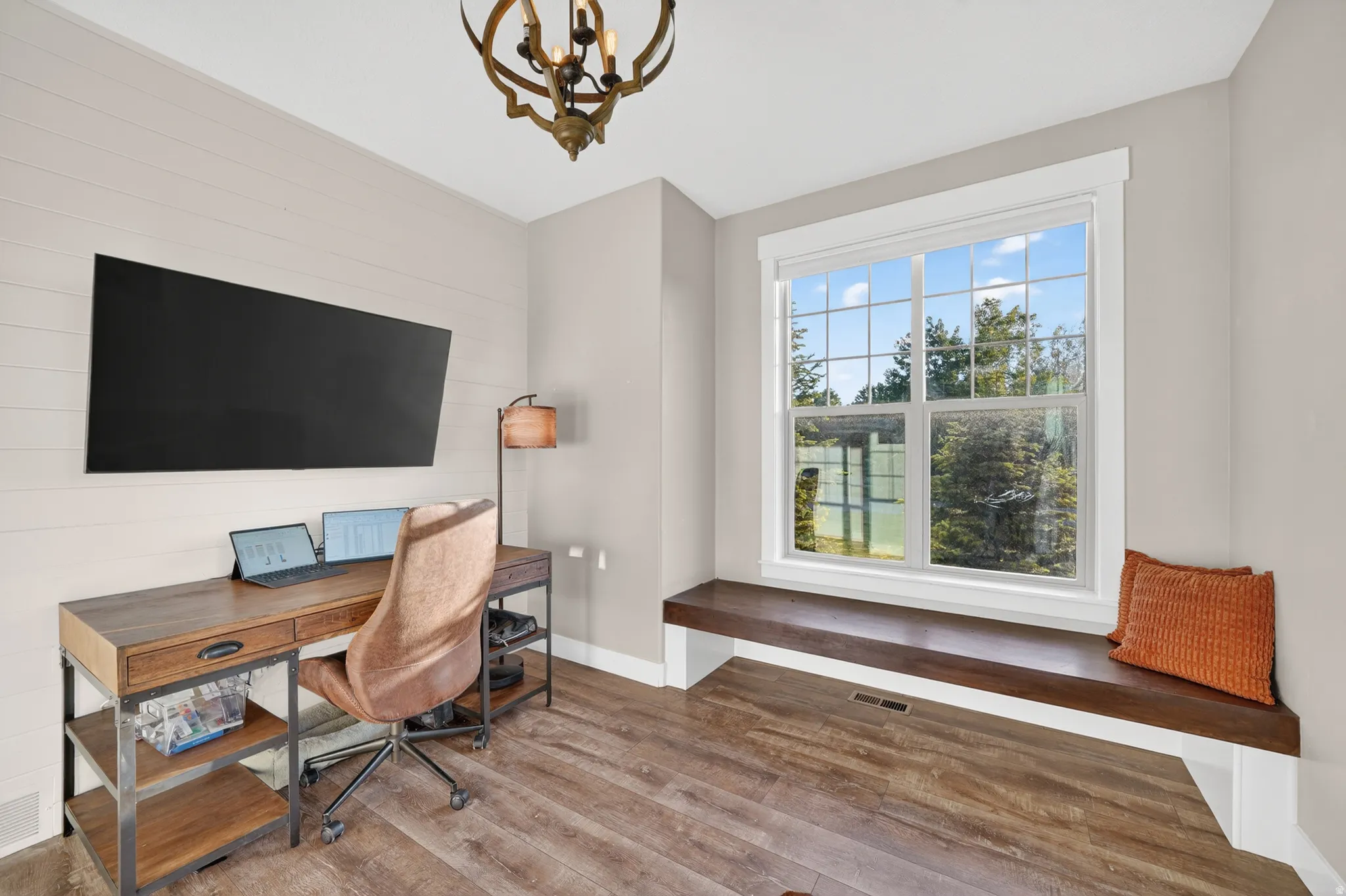 Room featuring a built-in window seat, large picture window, shiplap accent wall, and wood-finish flooring