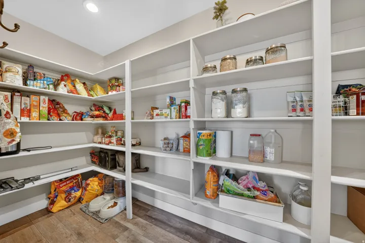 Spacious walk-in pantry featuring extensive white shelving, recessed lighting, and wood-finish flooring