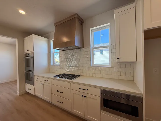 Kitchen featuring white shaker cabinetry, light countertops, subway tile backsplash, and wood-finish flooring