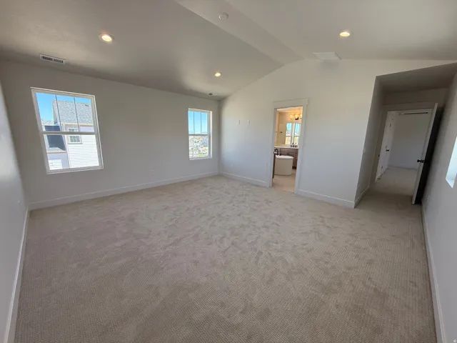 Spacious carpeted room featuring a vaulted ceiling with recessed lighting, multiple windows, and crisp white trim