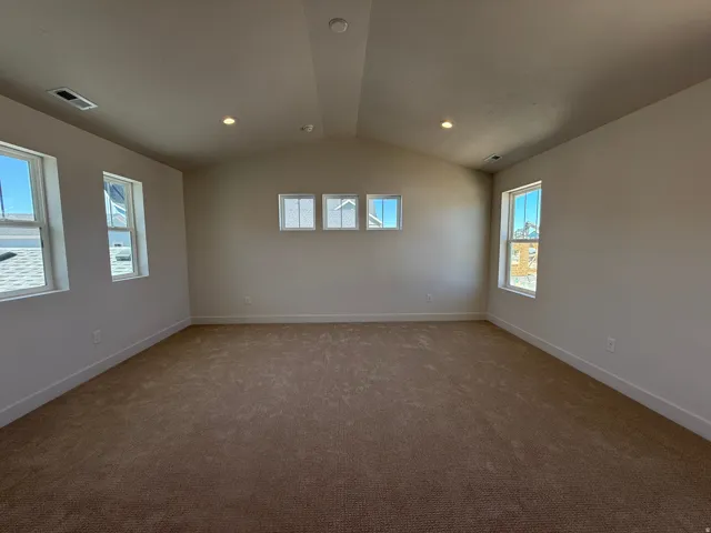 Spacious room featuring vaulted ceilings, recessed lighting, neutral-toned carpeting, and multiple windows providing ample natural light