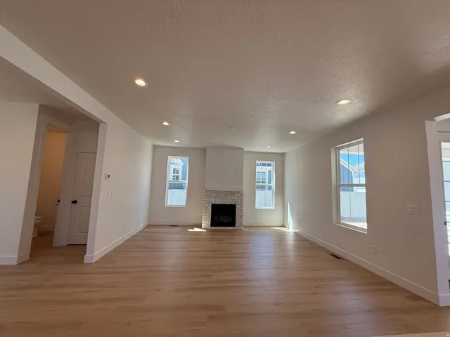 Open living area featuring wood-finish flooring, a white brick-surround fireplace, recessed lighting, multiple windows with white trim, and a bright white paint scheme
