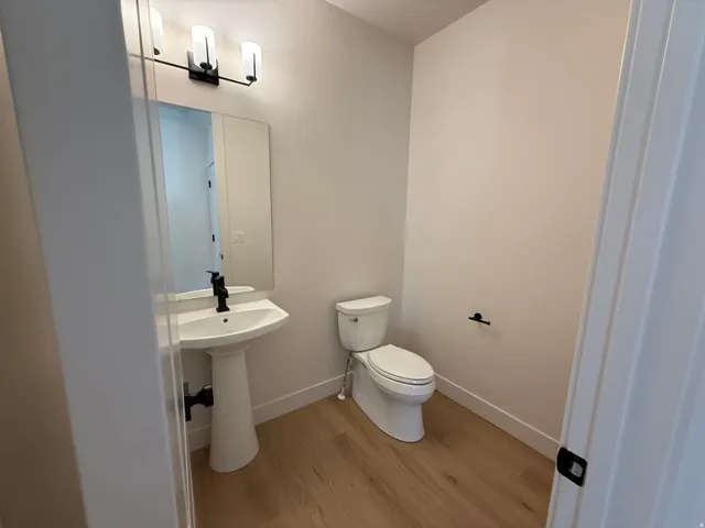 Bathroom featuring a pedestal sink with a matte black faucet, wall-mounted mirror, and a three-light vanity fixture