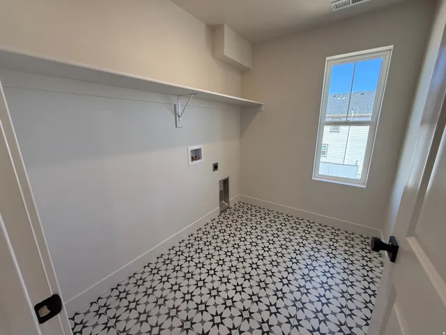 Dedicated utility room featuring patterned floor tiles, a single-pane window, and an integrated shelf with support brackets