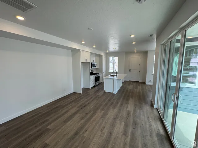 Open-concept living space with wood-finish flooring, recessed lighting, white walls, and a sliding glass door leading to an outdoor area