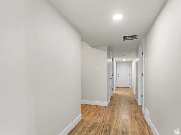 Hallway featuring wood-finish flooring, white baseboards, recessed lighting, and light-toned walls