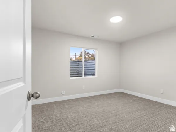 Carpeted room featuring a window with a window well, recessed lighting, and a solid interior door with a brushed nickel knob