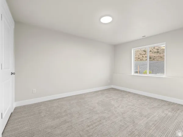 Neutral-toned room featuring a single window, light beige carpeting, a white door, and a circular ceiling light fixture