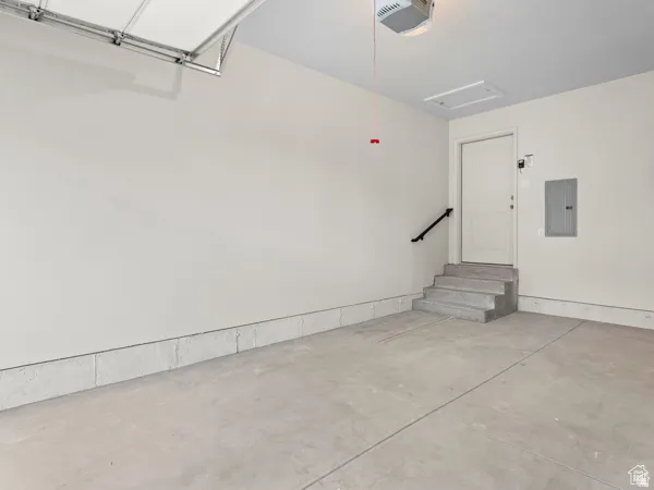 Spacious garage featuring a concrete floor, light-toned walls, an overhead garage door mechanism, and interior access via a staircase with a handrail