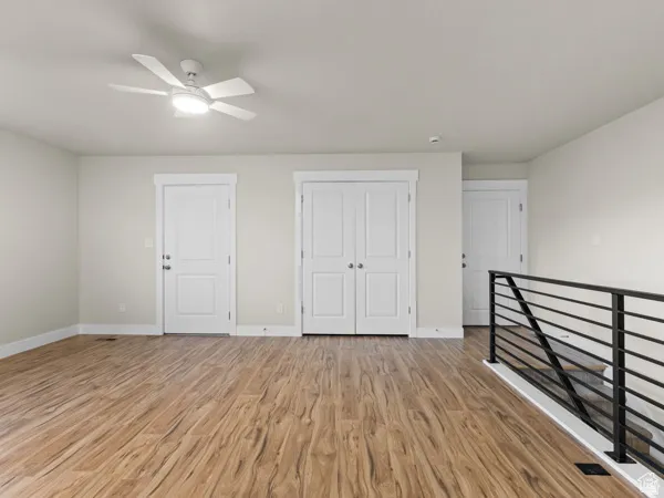Spacious open area featuring wood-finish flooring, a contemporary ceiling fan with integrated lighting, and a modern black metal railing