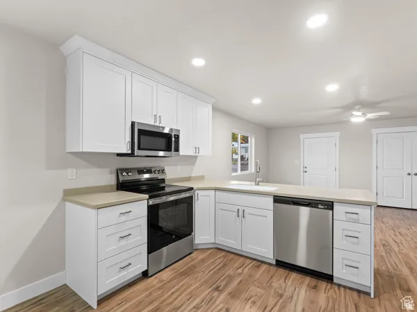 Modern kitchen featuring white shaker cabinetry, stainless steel appliances, light-toned countertops, wood-finish flooring, and recessed lighting