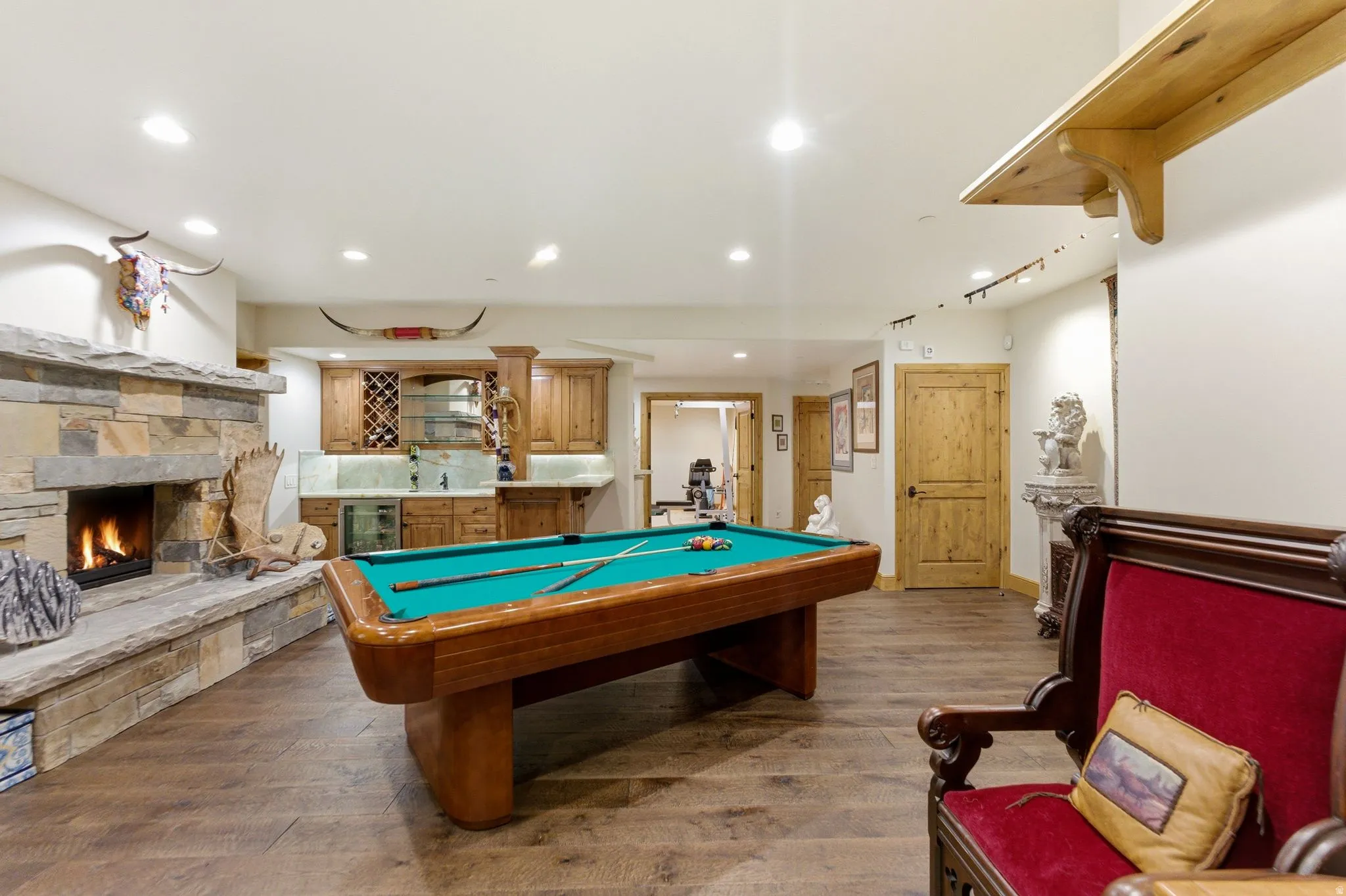 Recreation room featuring a natural stone fireplace, wood-finish flooring, a built-in wet bar with wood cabinetry, recessed lighting, and solid wood doors