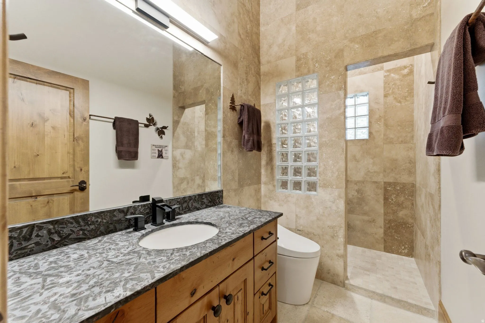 Bathroom featuring a wood vanity with a stone countertop, a white undermount sink, and matte black fixtures