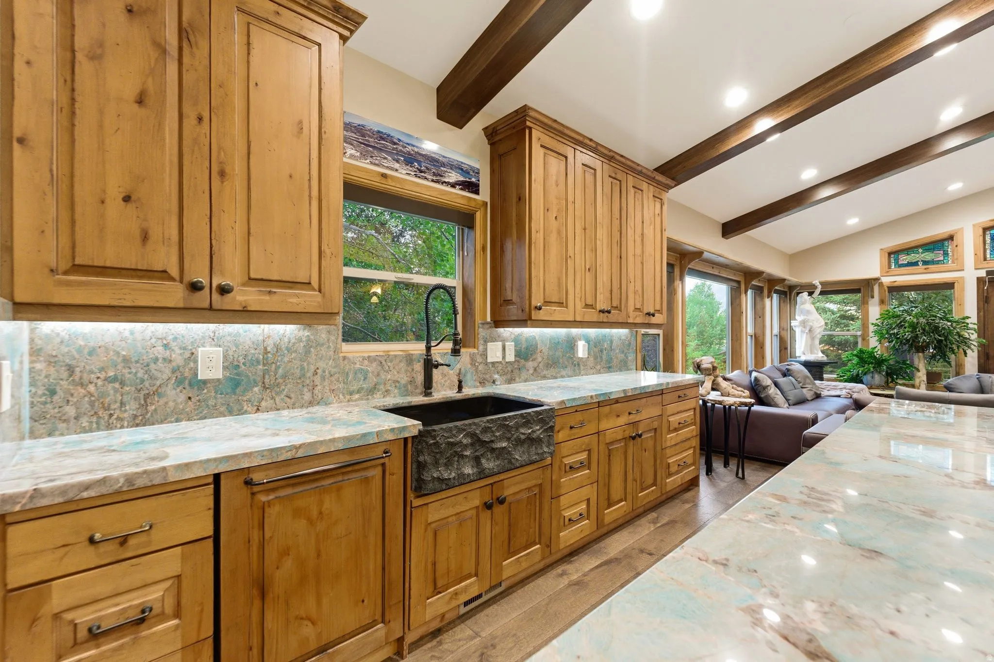 Kitchen featuring custom wood cabinetry, stone countertops, a large farm sink with a dark-finish faucet, and a coordinating stone backsplash