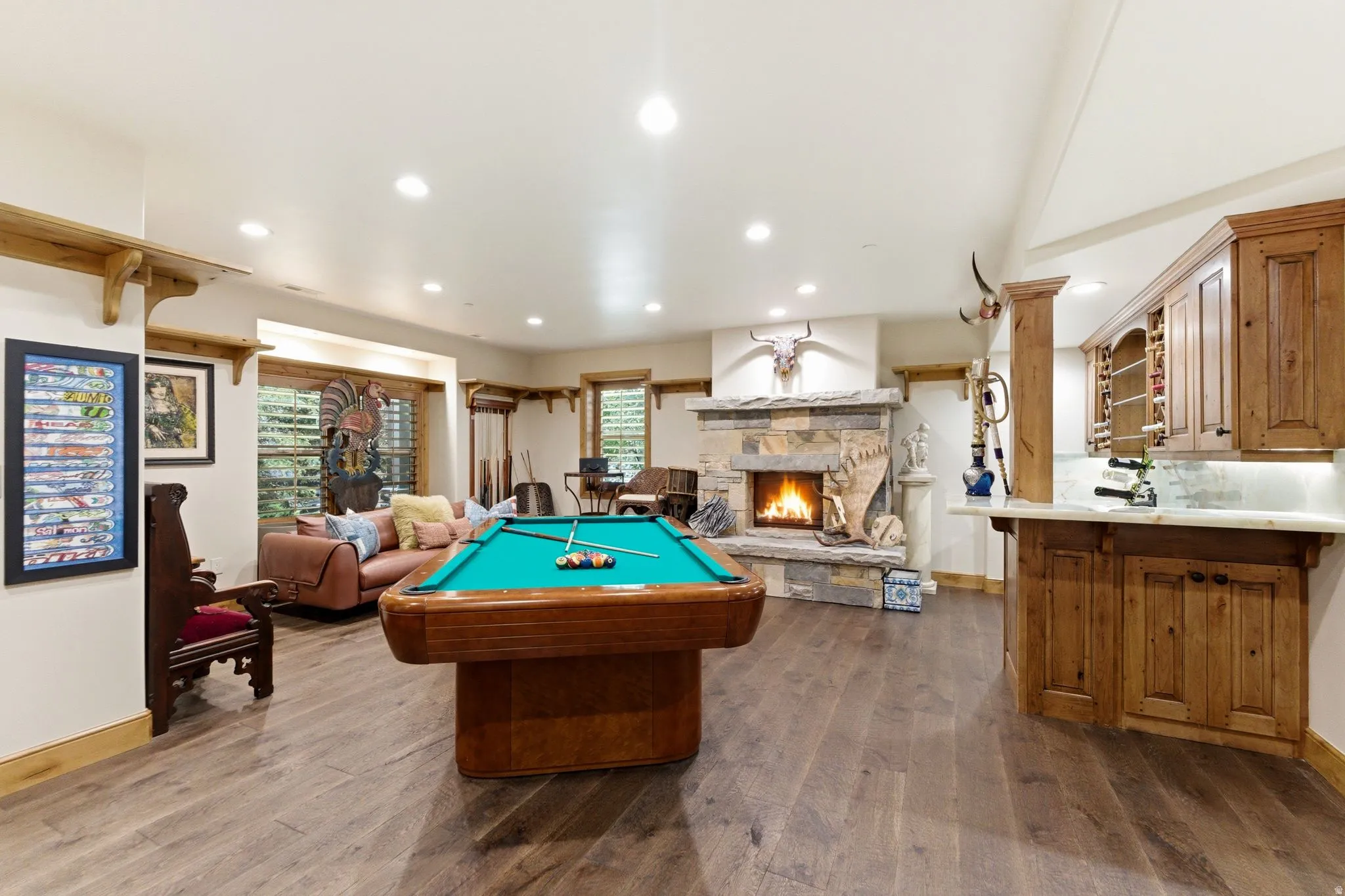 Spacious entertainment area featuring wood-finish flooring, a stone fireplace, recessed lighting, a built-in wet bar with wood cabinetry, and a pool table