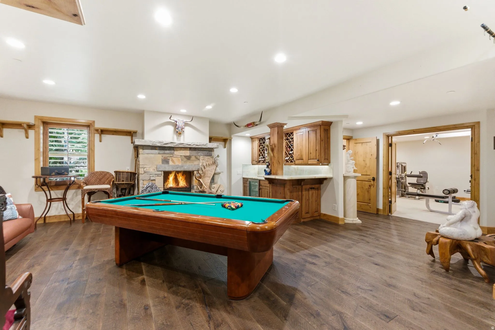 Spacious recreation room featuring wood-finish flooring, a stone fireplace, and a built-in wet bar with cabinetry