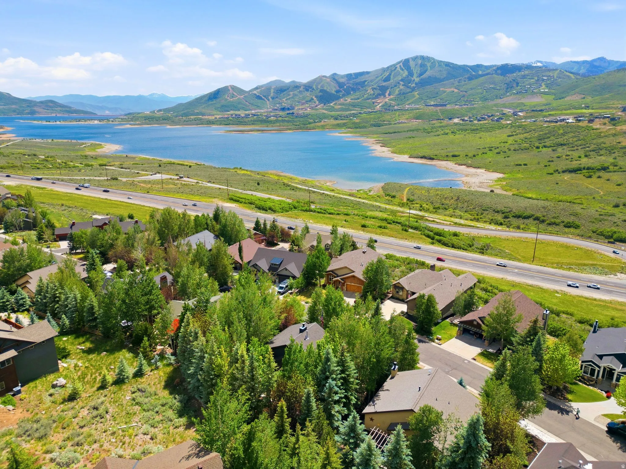 Mountainous landscape featuring a prominent lake, green hillsides, and a residential area with mature trees and paved roads