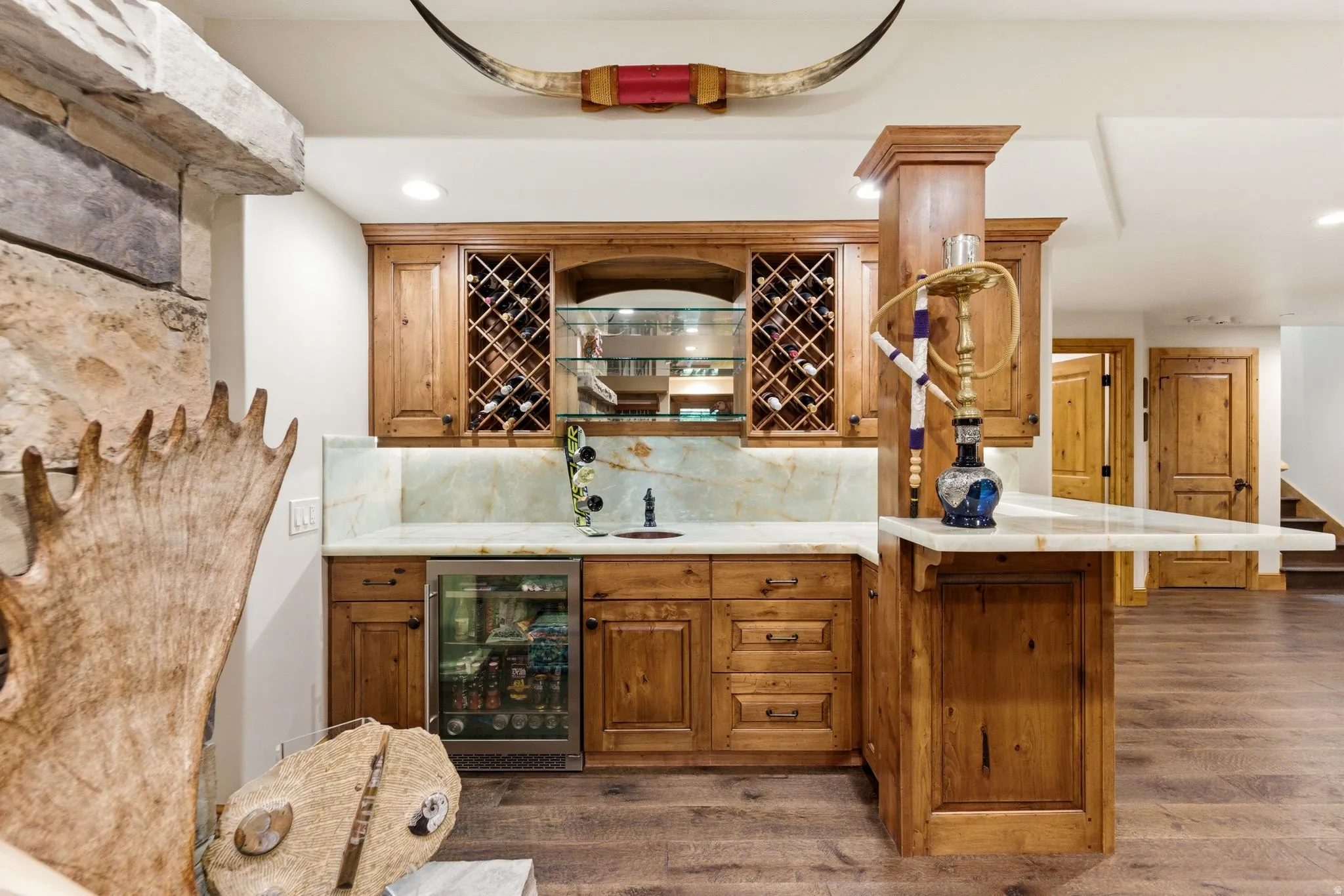 Custom wet bar featuring wood cabinetry, integrated wine storage, under-cabinet lighting, a beverage refrigerator, and stone countertops with a matching backsplash