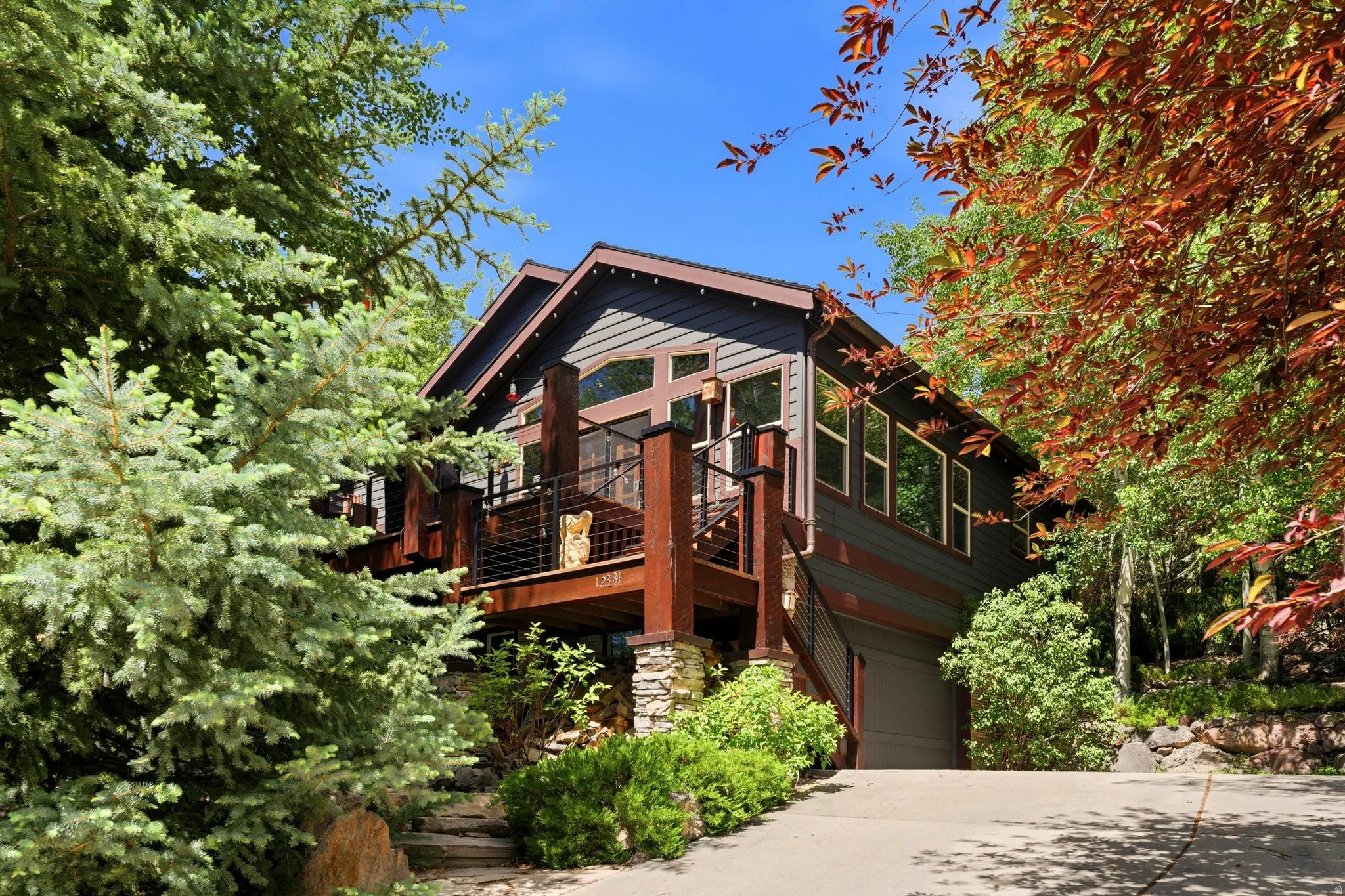 Multi-level residence featuring dark siding, a prominent wood deck with metal cable railing, and a stone-clad lower level